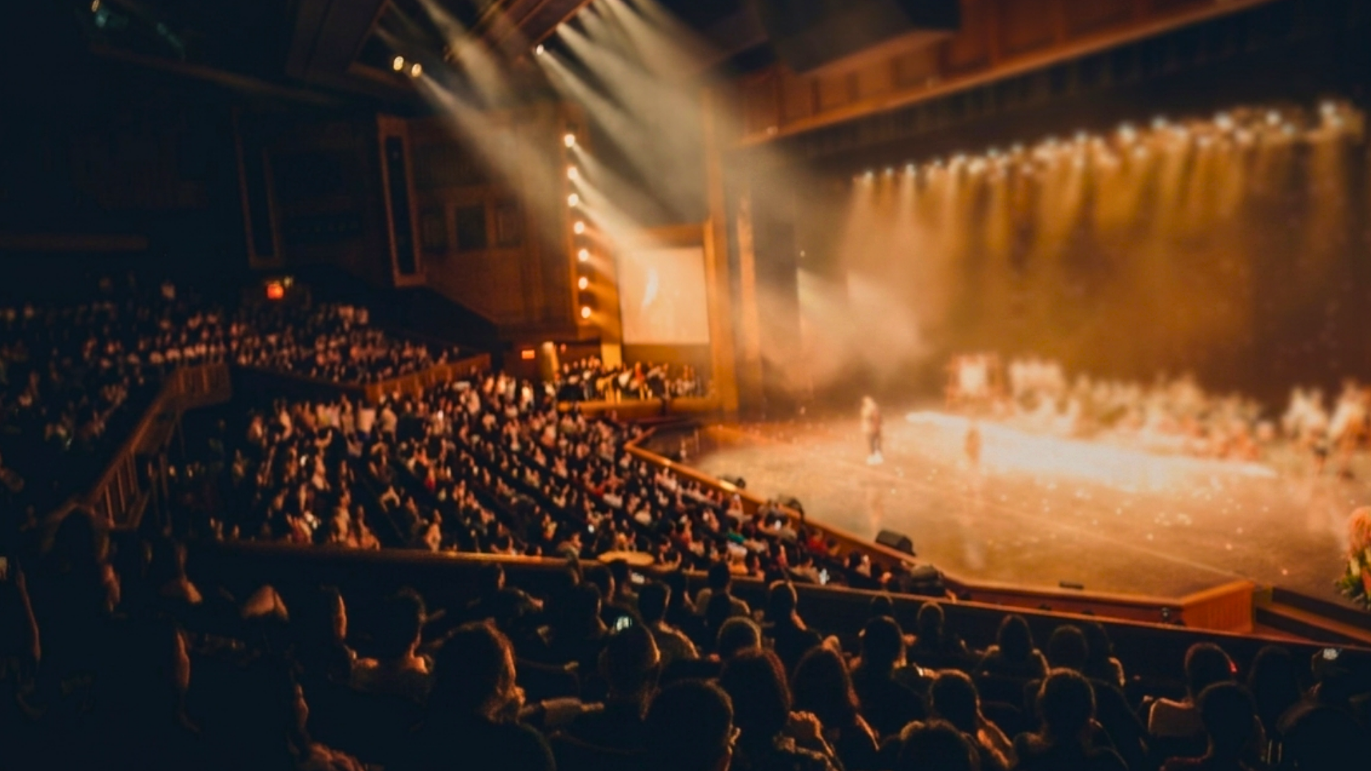 Sfeerbeeld theaterzaal, links zie je publiek in stoelen rechts een podium dat belicht wordt